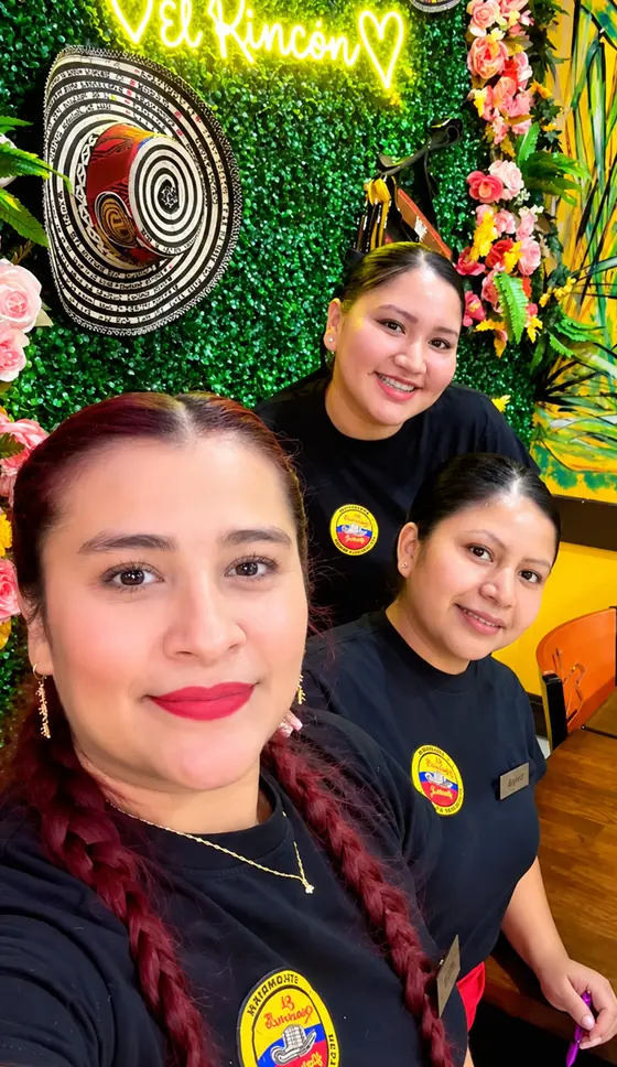 Servers at El Rinconcito Paisa 2 by the El Rincon neon sign and sombrero vueltiao wall